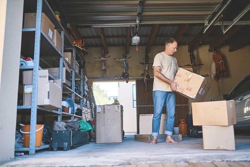 Mann verräumt Kisten in einer vollgestellten Garage 