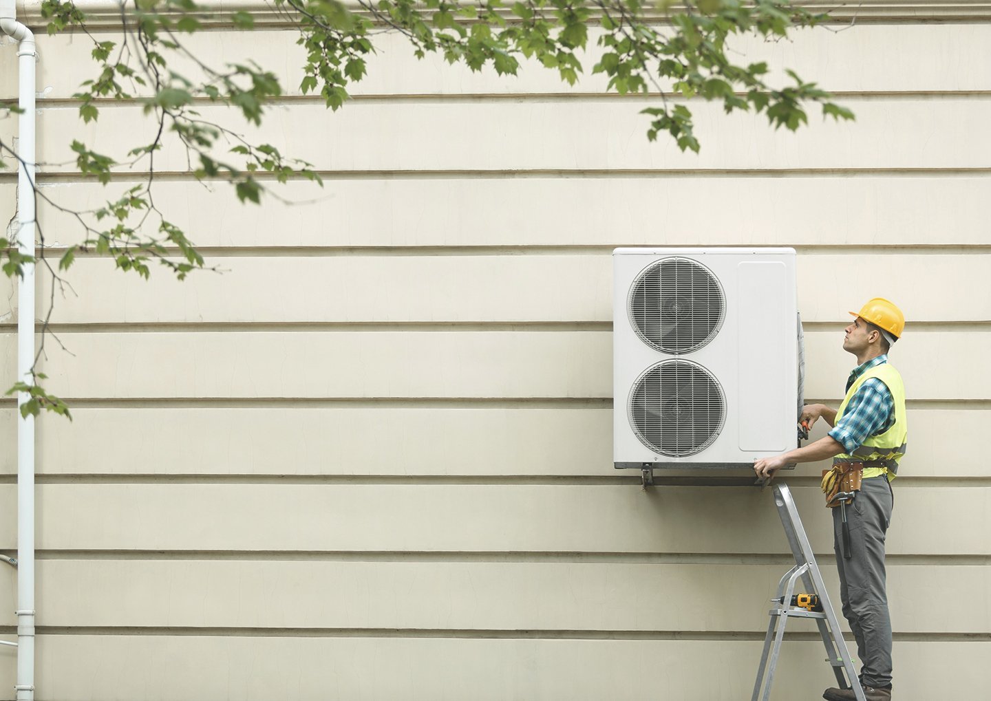 Bauarbeiter montiert Wärmepumpe an eine Häuserwand