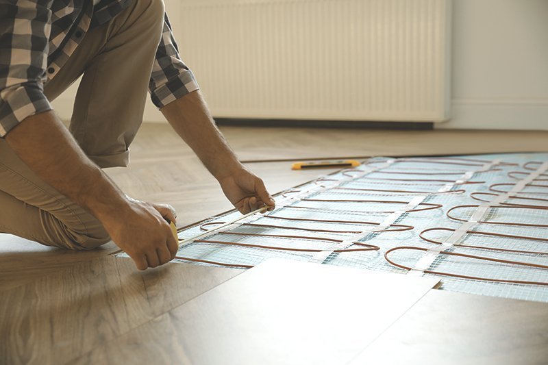Eine Person kniet auf Vinylboden und verlegt eine elektrische Fußbodenheizung
