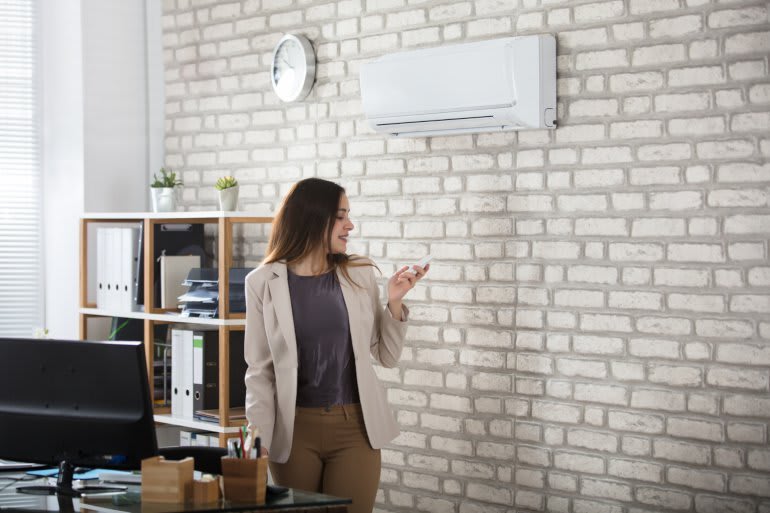 Frau bedient an der Wand hängende Split-Klimaanlage 
