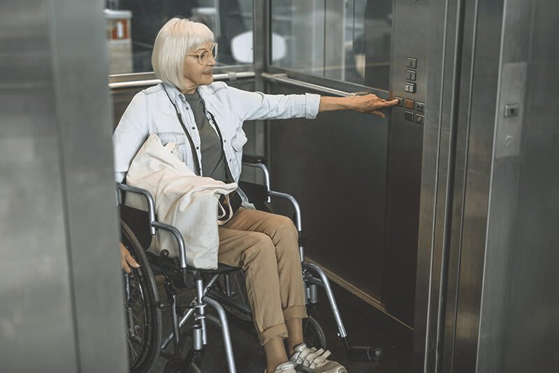 Ältere Frau mit Rollstuhl im Lift