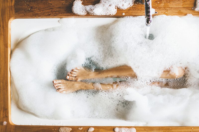 Frau badet mit viel Schaum in einer Eckbadewanne