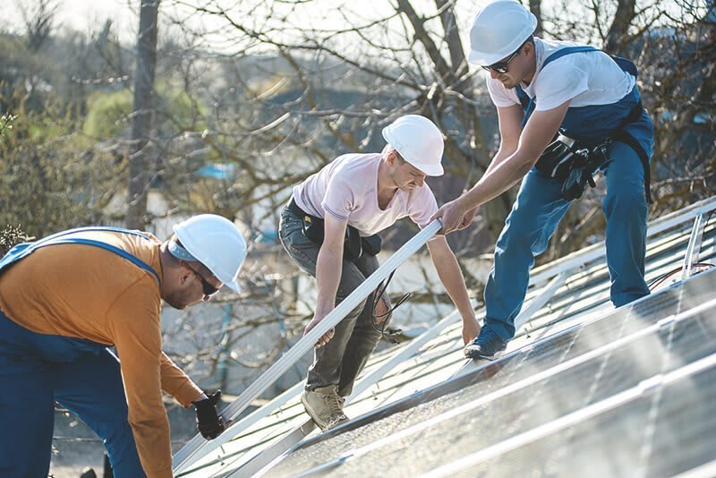 Drei Bauarbeiter auf Dach mit Solaranlage