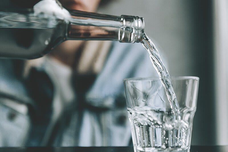 Wasser wird aus Glasflasche in Glas eingegossen