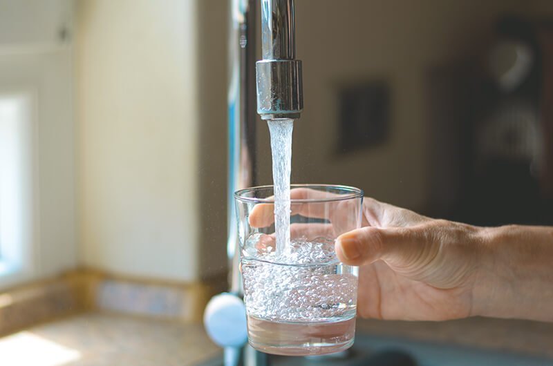 Wasserglas wird am Wasserhahn aufgefüllt